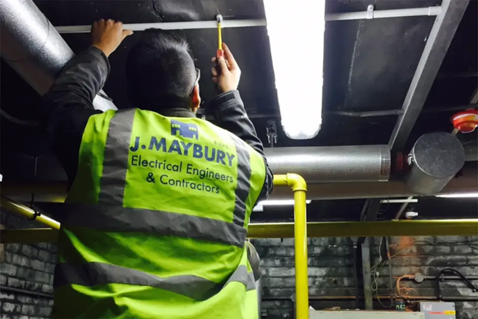 J Maybury electrician in a branded hi-vis vest working on ceiling wiring